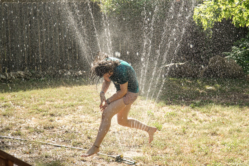 Kind springt durch den Wasserstrahl eines Viereckregners